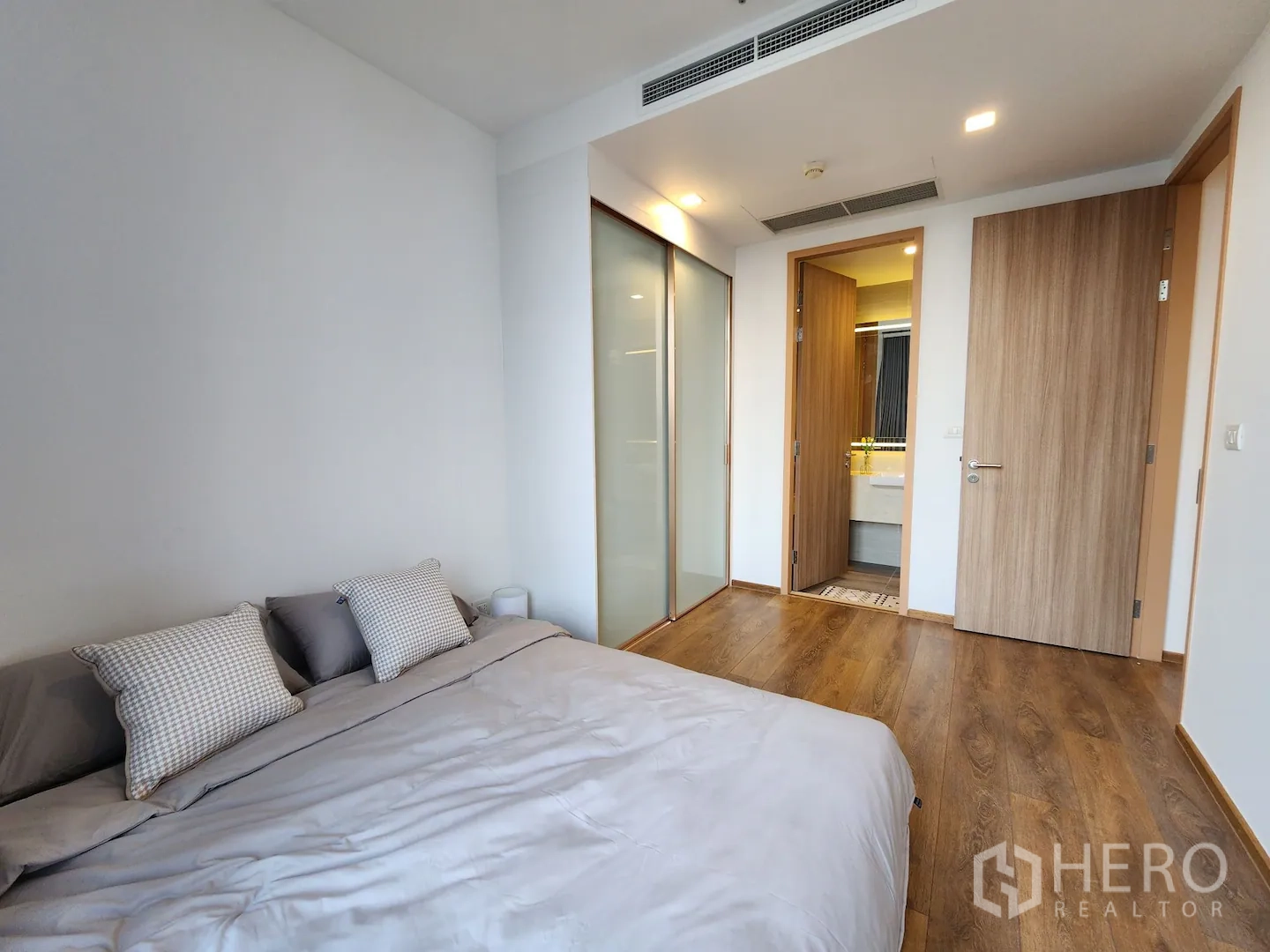 Condominium for rent in Watthana, Bangkok - Primary bedroom with wood floors, sliding wardrobe and doorway to a modern bathroom in a Watthana Bangkok condo.