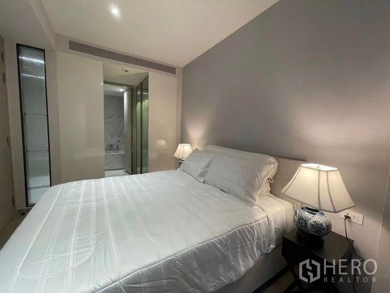 Condominium for rent in Khlong Toei, Bangkok - Bedroom with white bedding, bedside lamps and access to bathroom