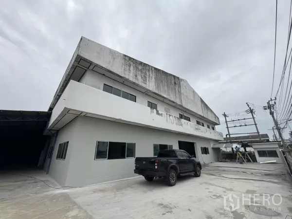 Factory for rent in Khlong Toei, Bangkok - Side exterior of the factory showing a wide concrete yard and ongoing repainting.