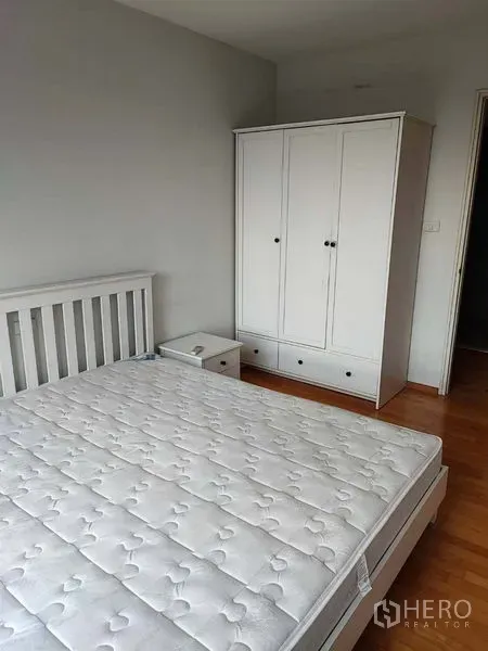 Condominium for sale in Khlong Toei, Bangkok - Second bedroom with white bed frame, wardrobe and bedside table on wood flooring.