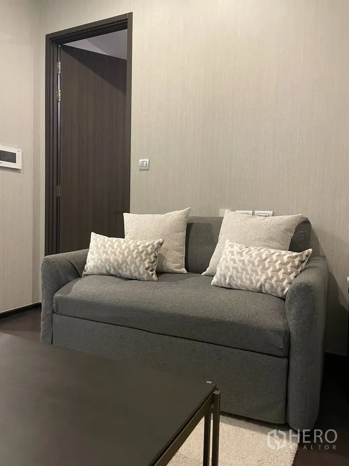 公寓 for rent in Watthana, Bangkok - 起居区灰色双人沙发与抱枕，旁为深色木门。