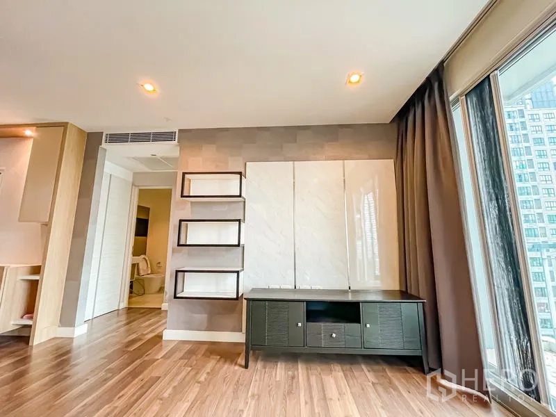 Condominium for sale - Media wall with floating shelves and TV console opposite full-height windows.