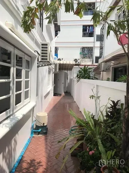 独立式住宅 出租在Khlong Toei, Bangkok - 白色房屋旁的砖铺侧院通道，带窗户、空调室外机和盆栽