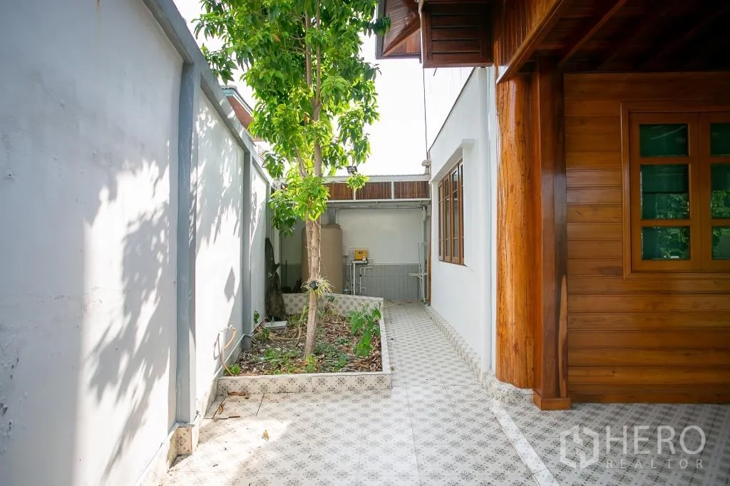 独栋房屋 for rent or sale in Huai Khwang, Bangkok - 侧院步道铺花砖，带小花坛与设备区，靠白色围墙。