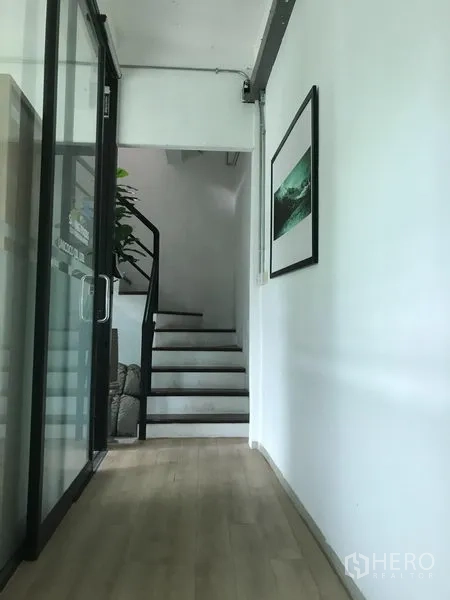店屋 出租在Watthana, Bangkok - 走廊设玻璃墙与浅木地板，尽头为通往楼上的楼梯