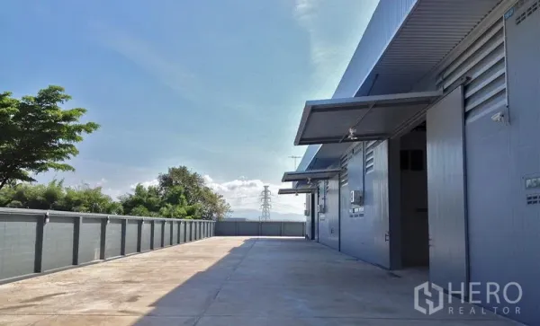 Warehouse for rent in Si Racha, Chon Buri - Fenced service road along the warehouse with loading bays and clear blue sky.