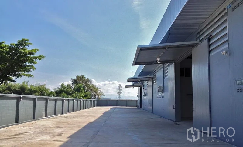 Warehouse for rent in Si Racha, Chon Buri - Fenced service road along the warehouse with loading bays and clear blue sky.