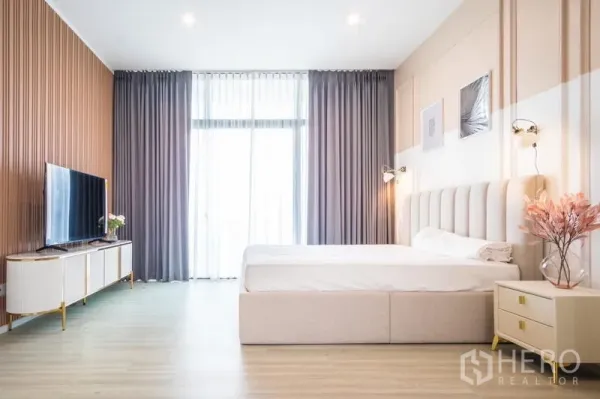 Townhouse for rent or sale in Suan Luang, Bangkok - Bright master bedroom with king bed, floor-to-ceiling curtains, and a sleek TV console.