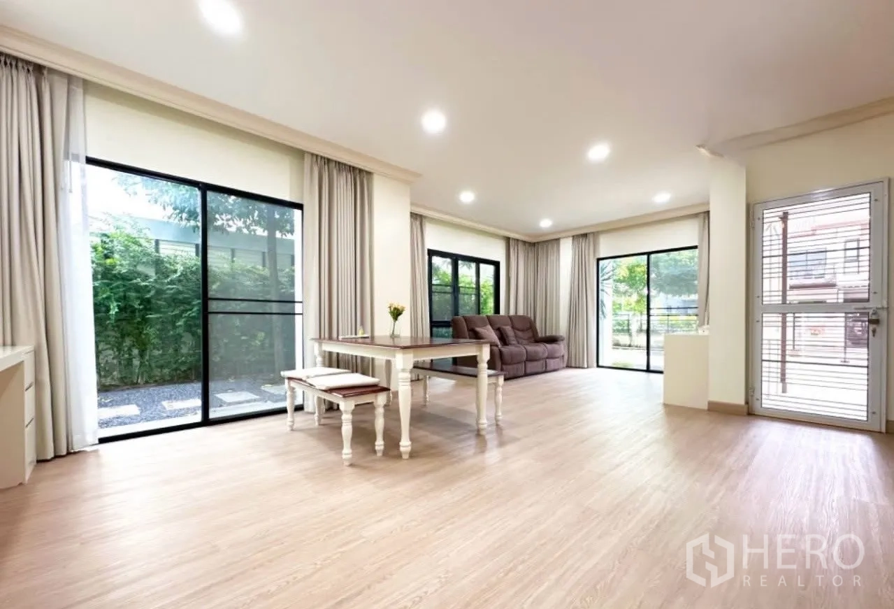Detached House for sale in Lam Luk Ka, Pathum Thani - Bright lounge and dining space with sliding glass doors on two sides and light wood flooring.