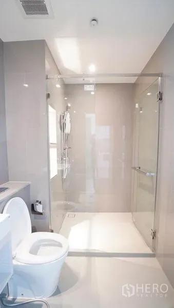 Condominium for sale in Khlong Toei, Bangkok - Bright modern bathroom with a glass-enclosed walk-in shower, rainfall head and white fixtures.