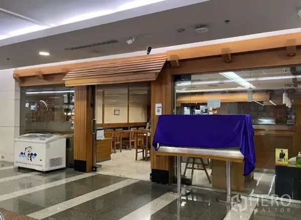 零售空间 出租在Phaya Thai, Bangkok - 商场内零售铺面，木质门头与落地玻璃门面，店内设座位，适合咖啡店或餐饮。