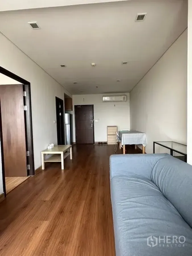 公寓 出售在Watthana, Bangkok - 宽敞客厅，木地板、灰色沙发、空调与入户门。