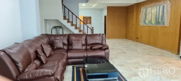 联排别墅 出租在Watthana, Bangkok - 宽敞客厅，棕色皮沙发、石纹地面与楼梯。