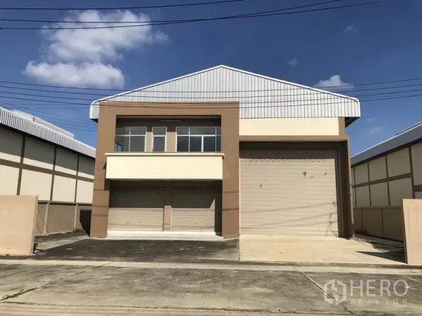 Factory for rent or sale in Pathum Thani - Front view of a modern mini factory with roller shutter doors, upper-floor office windows and a metal gable roof.