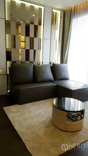 Condominium for rent in Watthana, Bangkok - Compact lounge with dark sectional sofa, mirrored accent wall and a round coffee table.