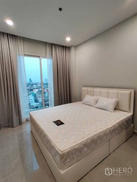คอนโด ให้เช่าในBang Rak, Bangkok - ห้องนอนเตียงบุนวม หน้าต่างบานใหญ่เห็นวิวเมือง ผ้าม่านสีเทา และไฟดาวน์ไลท์