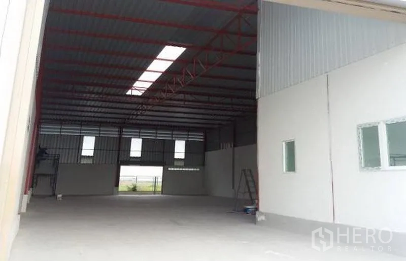 Factory for rent in Pathum Thani - High-ceiling warehouse with red steel trusses, skylight panels, and an internal office wall.