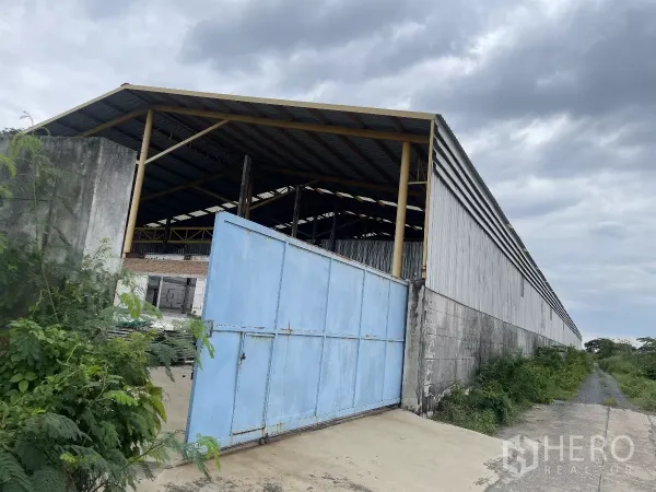 โรงงาน ขายในBang Bua Thong, Nonthaburi - ภายนอกโกดังผนังเมทัลชีท ประตูเหล็กสีน้ำเงินกว้าง ติดถนนทางเข้า