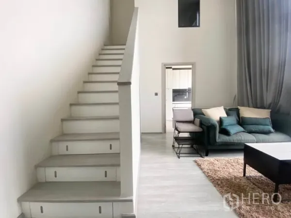 Condominium for rent in Phra Khanong, Bangkok - Staircase rising from the living area with sofa and rug, highlighting the high ceiling and tall windows.