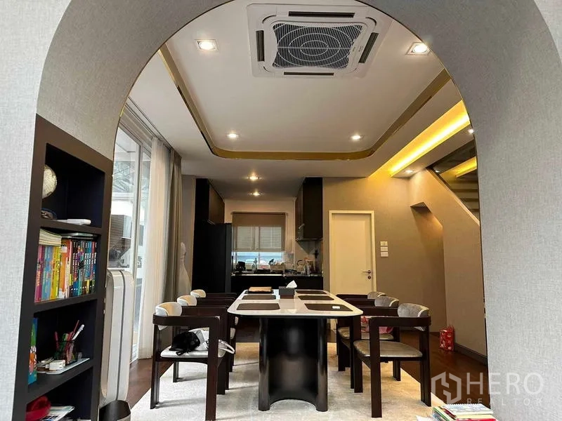 Detached House for sale in Suan Luang, Bangkok - Dining room under an arched opening with ceiling cassette AC and kitchen beyond.