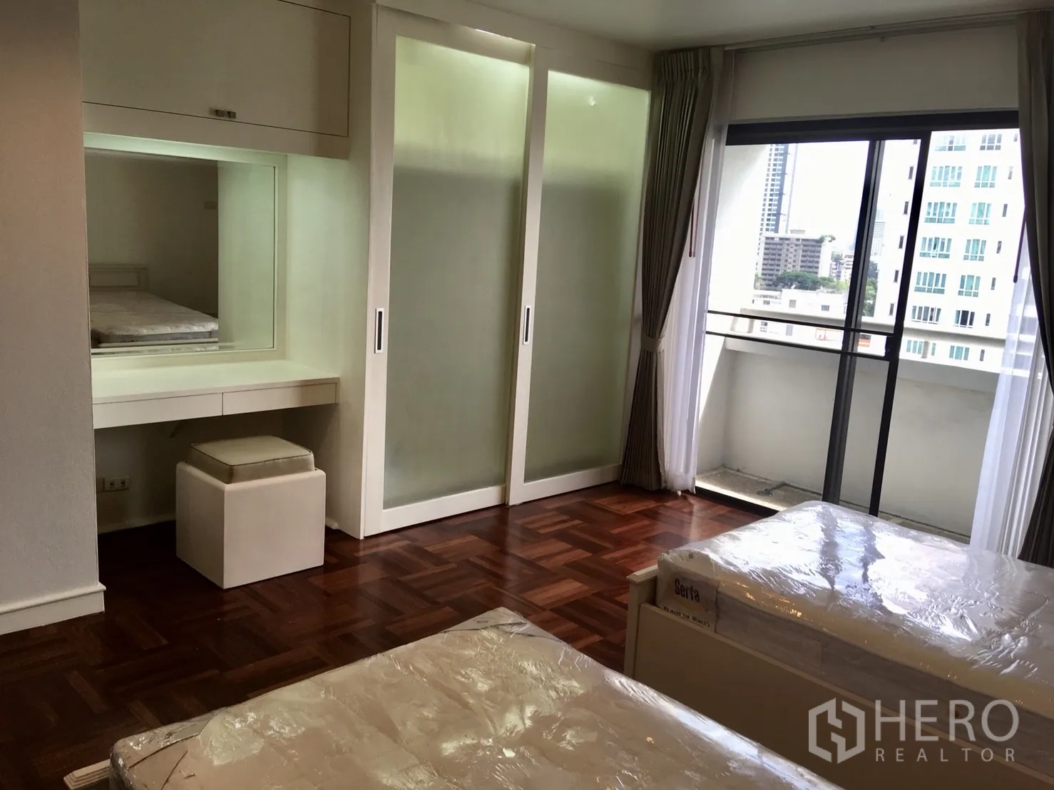 Condominium for rent or sale in Watthana, Bangkok - Bedroom with two beds, built‑in vanity and sliding door to a city‑view balcony.