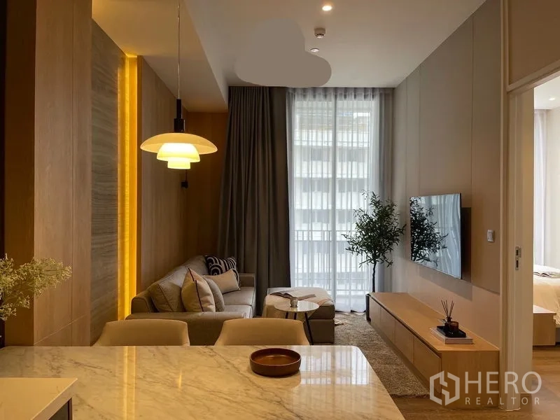 公寓 出租或出售在Pathum Wan, Bangkok - 从厨房望向客厅的视角，吊灯、落地窗与卧室入口一览。