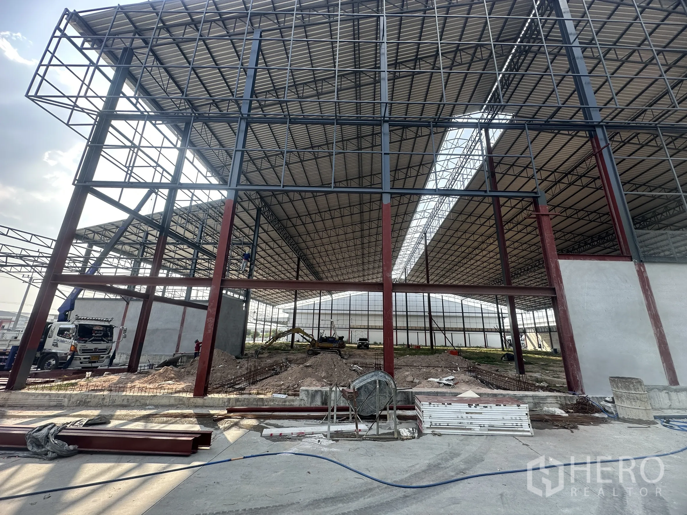工厂 for rent in Si Racha, Chon Buri - 高耸钢桁架屋顶与红色立柱构成的仓库空间正在施工。