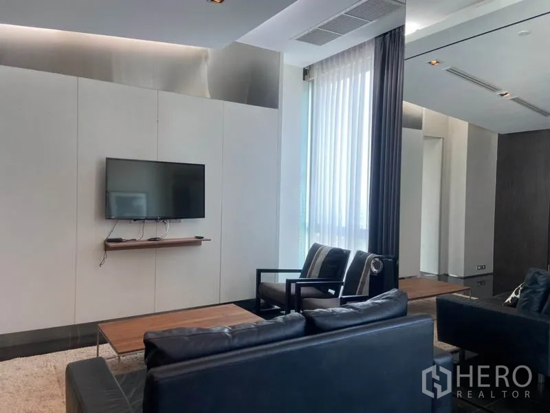 Condominium for rent in Sathon, Bangkok - Minimalist lounge with a wall-mounted TV, large curtained window and modern seating.