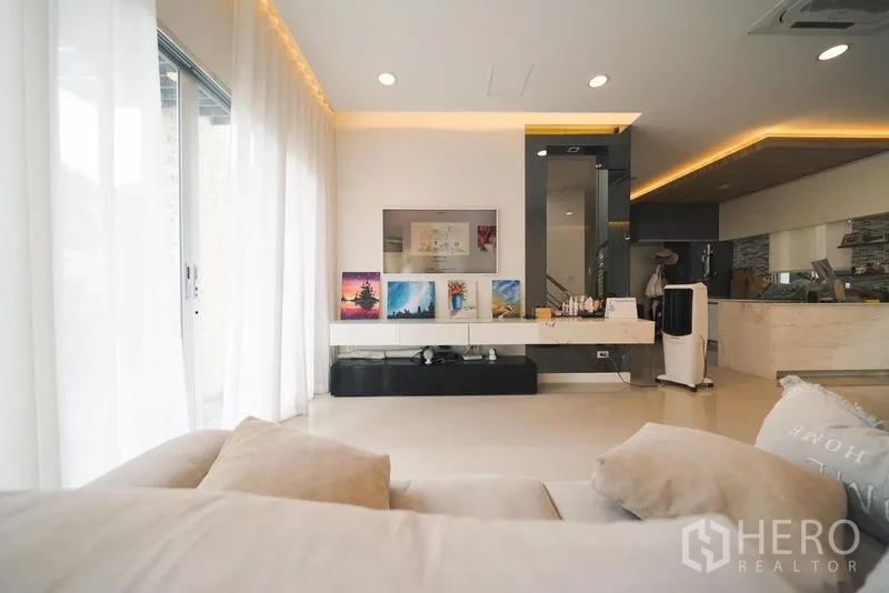 Detached House for rent or sale in Saphan Sung, Bangkok - Media wall with mounted TV, floating cabinet and floor‑to‑ceiling curtains beside sliding glass doors.