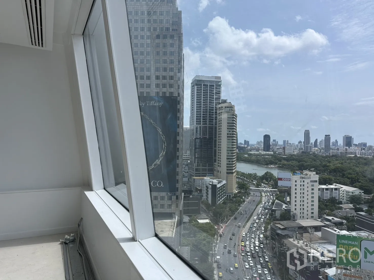 Office Space for rent in Watthana, Bangkok - City view through slanted glass, capturing high-rises, a lake, and a major road.