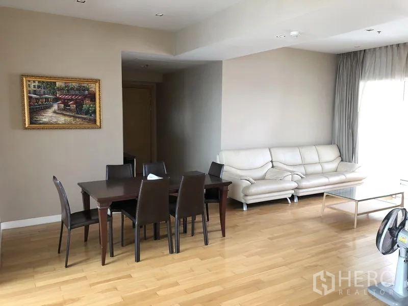Condominium for rent in Khlong Toei, Bangkok - Spacious dining space with a table for six and a cream leather sofa in the living room.