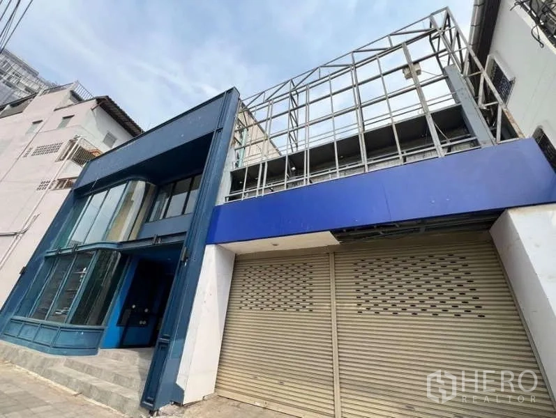 Retail Space for rent in Phaya Thai, Bangkok - Street view of blue shopfront with curved glass and adjacent rolling-door bay with sign frame.
