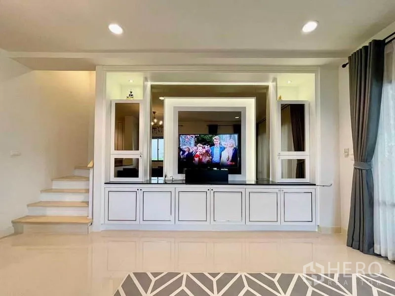 Townhouse for sale in Wang Thonglang, Bangkok - Built-in media wall with illuminated shelving and TV console beside the staircase in a bright living room.