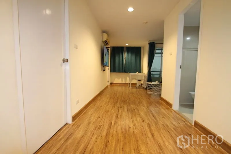 Condominium for rent or sale in Wang Thonglang, Bangkok - Bright corridor-style living area with wood floors, wall-mounted TV, and a dining nook by the window.