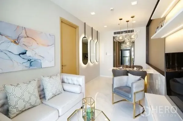 Condominium for rent in Watthana, Bangkok - Open-plan living and dining room with sofa and armchair, modern lighting, built-in shelving, and glossy floors.