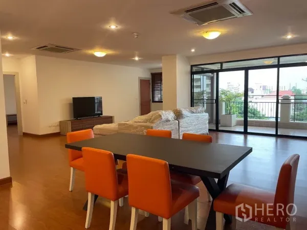 Condominium for rent in Watthana, Bangkok - Open-plan living and dining area with orange chairs, wood floors, and sliding doors to a balcony in an Ekkamai condo.