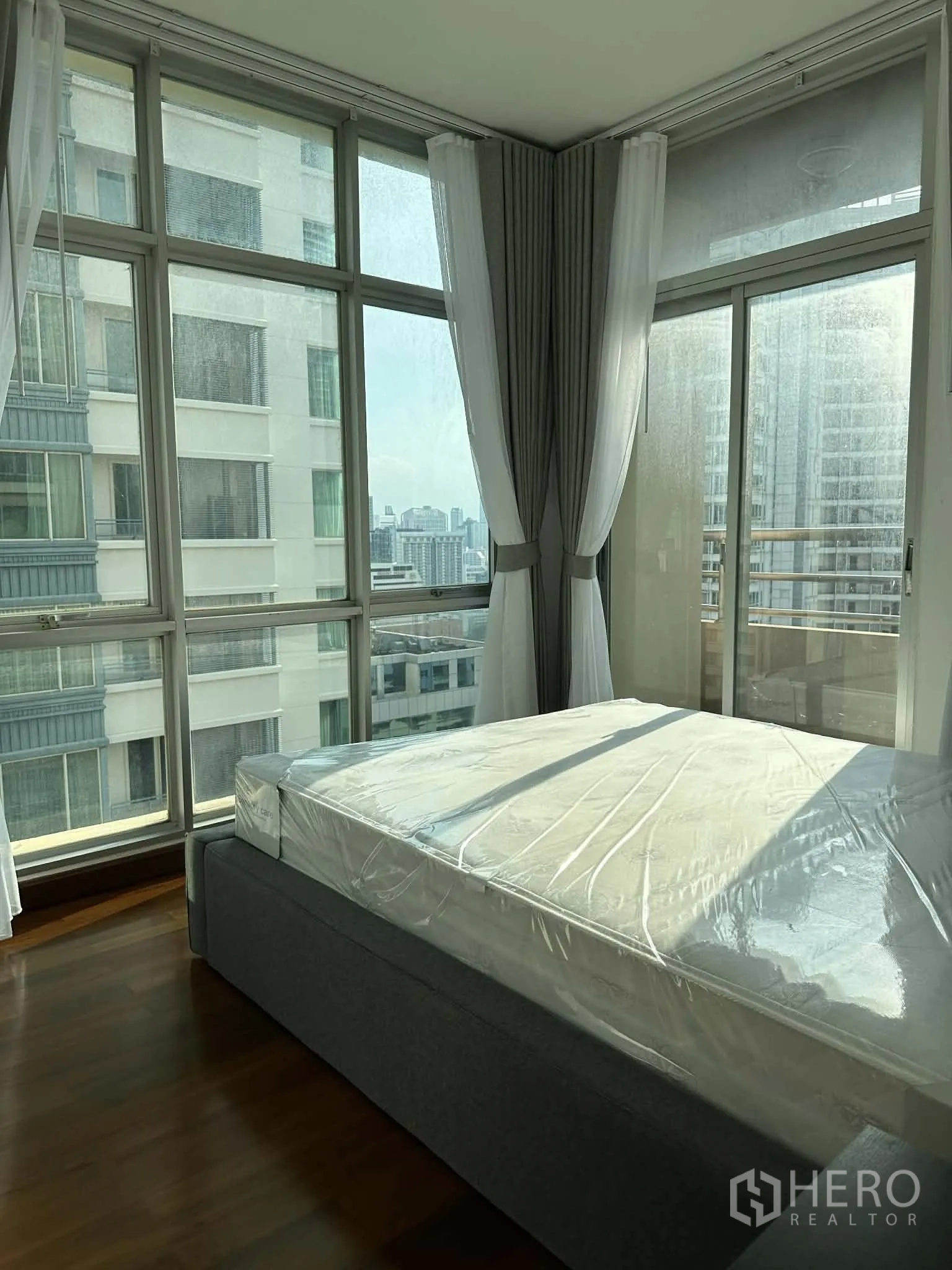 Condominium for rent in Pathum Wan, Bangkok - Corner bedroom with floor-to-ceiling windows and sheer curtains.