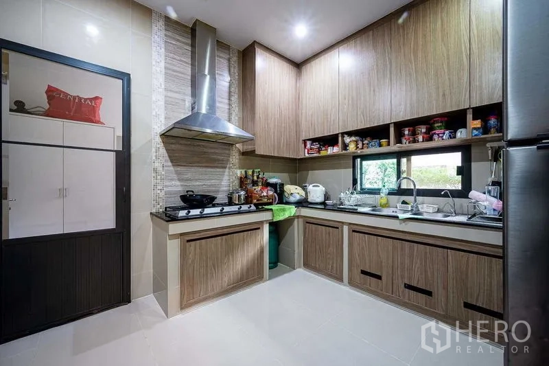 独立式住宅 出售在Prawet, Bangkok - 现代厨房，木质橱柜、燃气灶、不锈钢油烟机与水槽窗户。