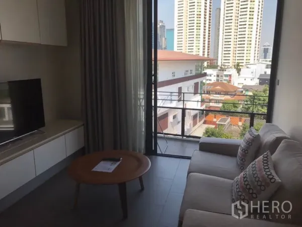 公寓 出租在Watthana, Bangkok - Ekkamai公寓客厅配沙发与电视，连接阳台，可欣赏城市景观。