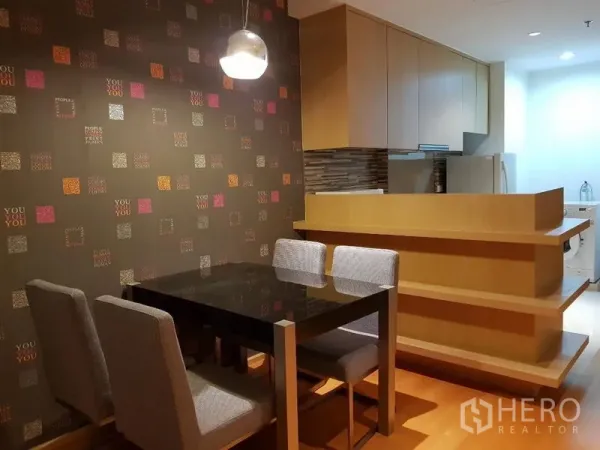 公寓 出租在Ratchathewi, Bangkok - 近景餐区与图案墙面，旁为浅木色厨房吧台并可见洗衣区域。