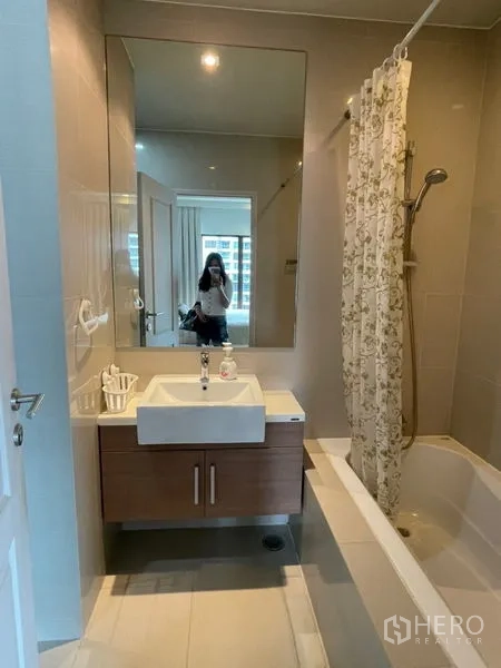 Condominium for rent in Bangkok - Clean bathroom with large mirror, curtain and shower-over-bathtub.
