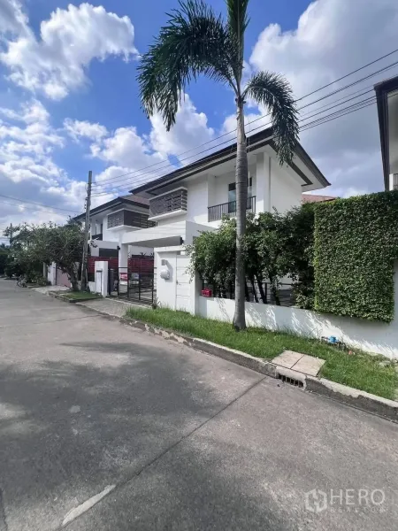 บ้านเดี่ยว for rent or sale in Saphan Sung, Bangkok - บ้านเดี่ยวสองชั้นสไตล์โมเดิร์นพร้อมรั้วหน้าและถนนมีต้นปาล์มเรียงราย.