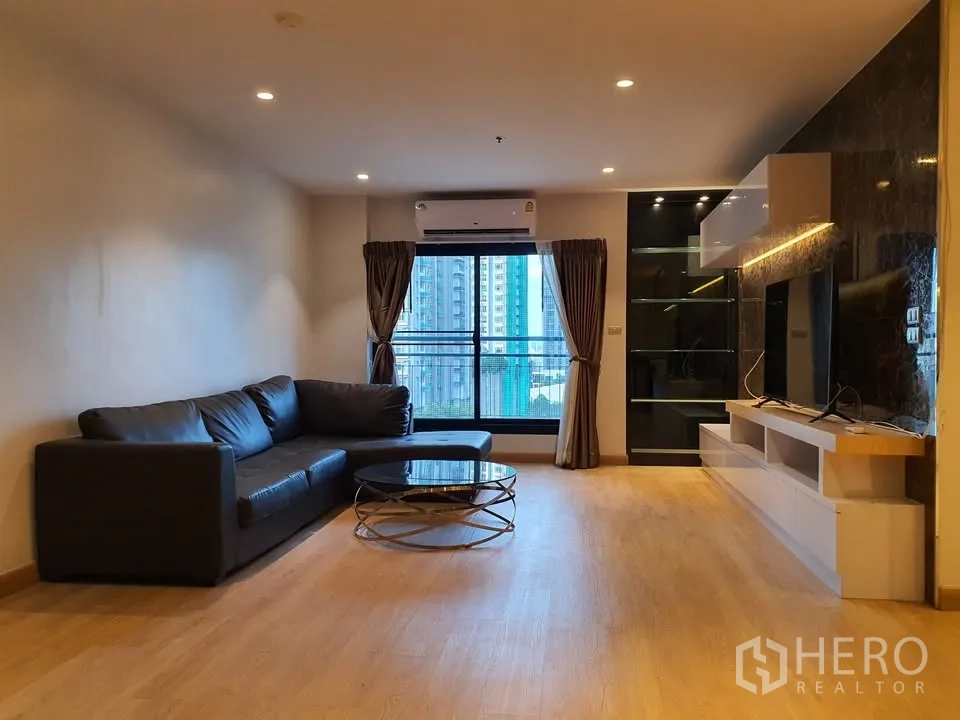 คอนโด for rent in Watthana, Bangkok - ห้องนั่งเล่นโซฟาหนังรูปตัวแอล โต๊ะกลางกระจก และระเบียงชมวิวเมือง