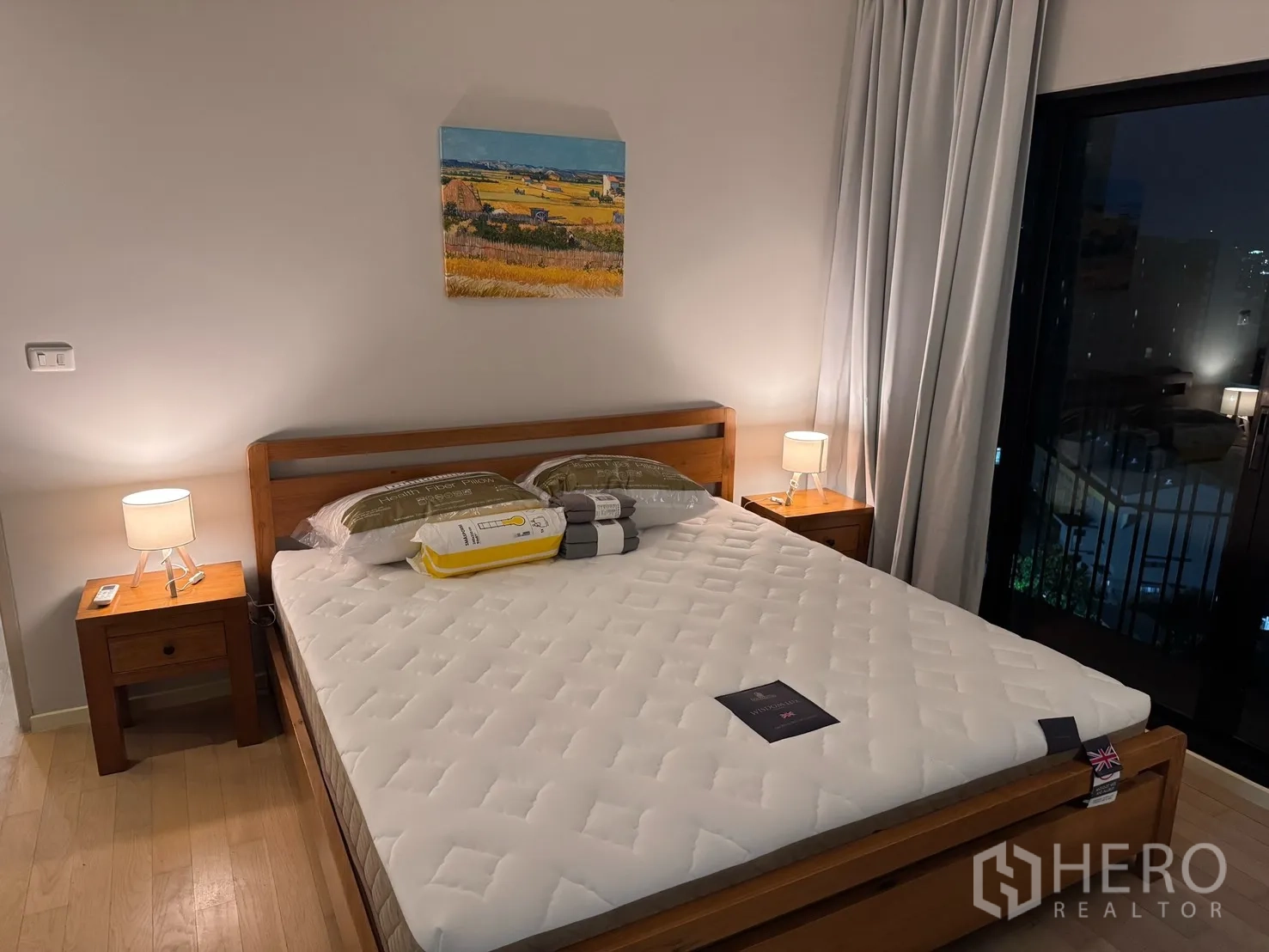 公寓 for rent or sale in Watthana, Bangkok - 主卧另一角度，展示床、床头柜与灯，以及带窗帘的玻璃门通往阳台。