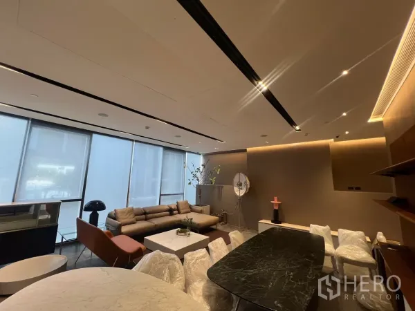 零售空间 出租 - 宽阔视角展示长沙发、卷帘、氛围灯带与深色石面餐桌，地面为石质砖。