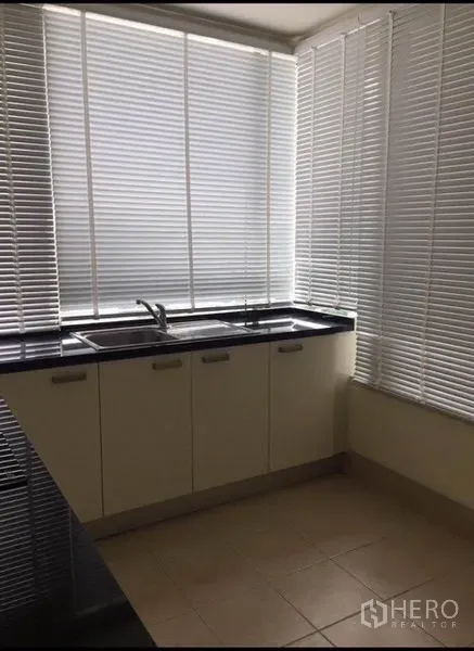 Condominium for rent in Watthana, Bangkok - Corner kitchen with white cabinets, black countertop and blinds filtering daylight.