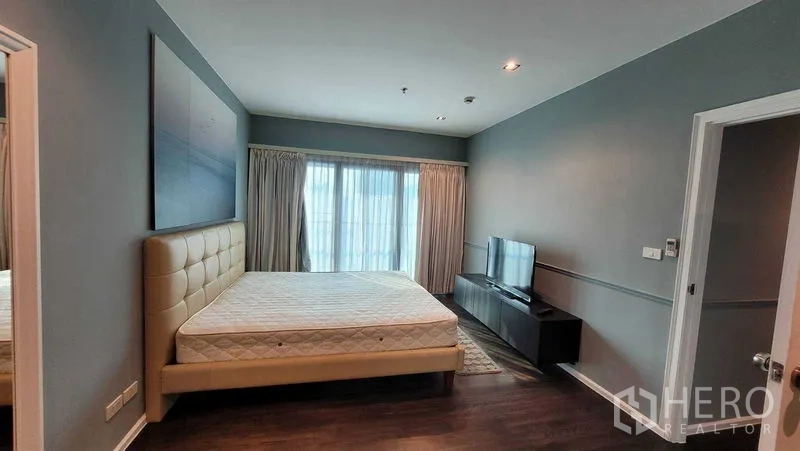 Condominium for rent in Khlong Toei, Bangkok - Master bedroom facing balcony doors with TV console and recessed lighting over dark wood floors.