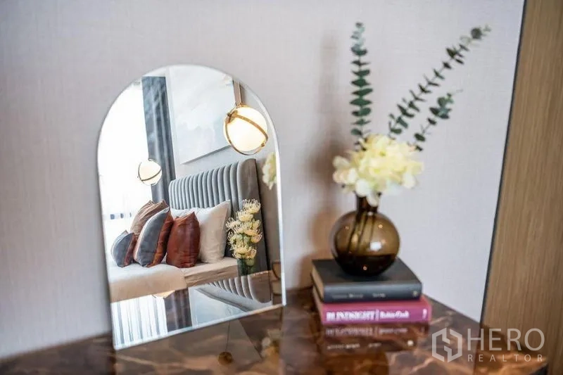 Condominium for rent in Khlong Toei, Bangkok - Decor vignette featuring an arched mirror and vase reflecting a cozy bedroom scene.