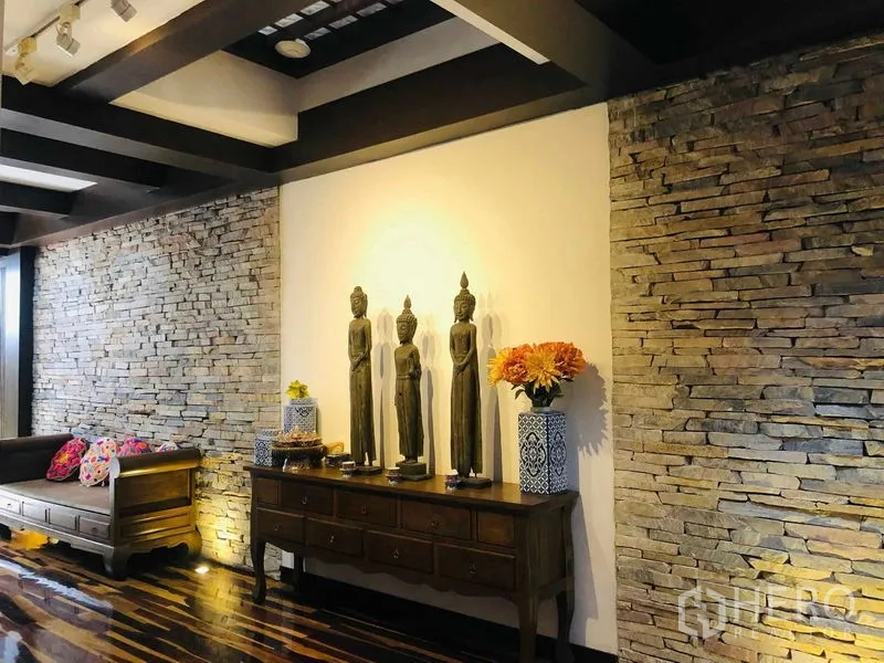 Townhouse for rent in Yan Nawa, Bangkok - Hallway vignette with a wooden console, decorative statues, and textured stone walls.