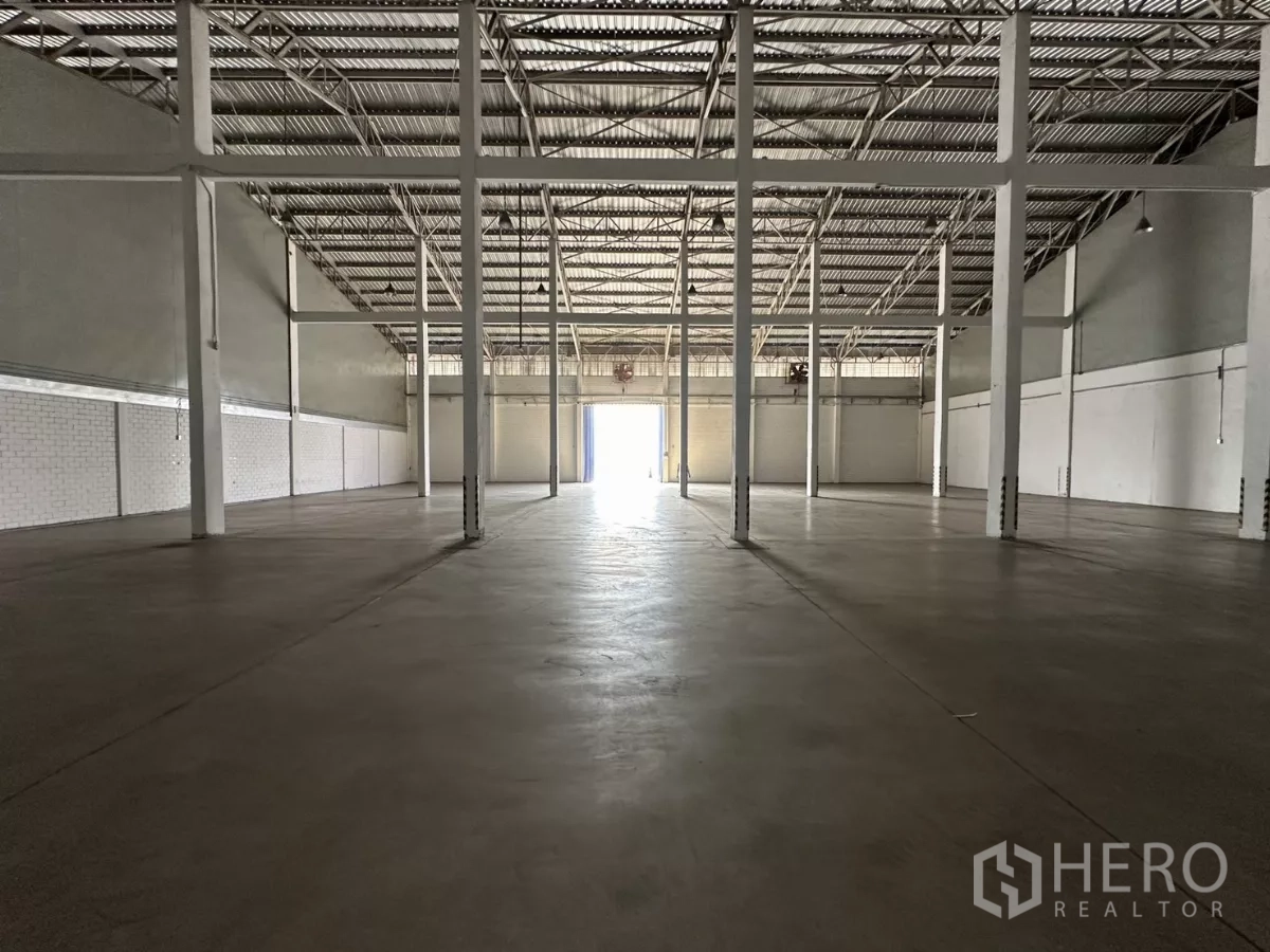 Warehouse for rent in Phra Khanong, Bangkok - Empty warehouse interior with high steel roof, concrete floor and multiple columns.